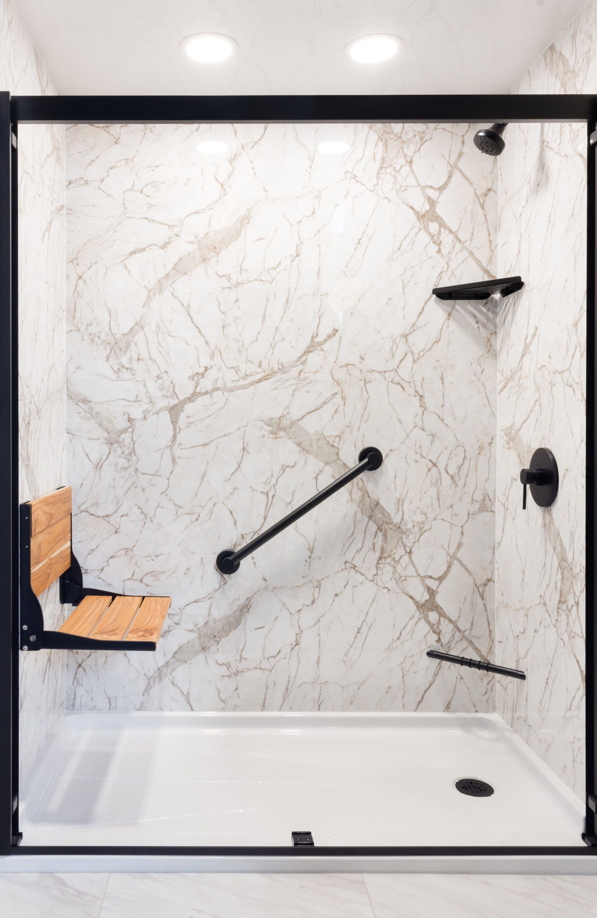 Modern shower enclosure with cream marble walls, black framed glass door, black fixtures including showerhead and grab bars, white base, and wooden bench seat