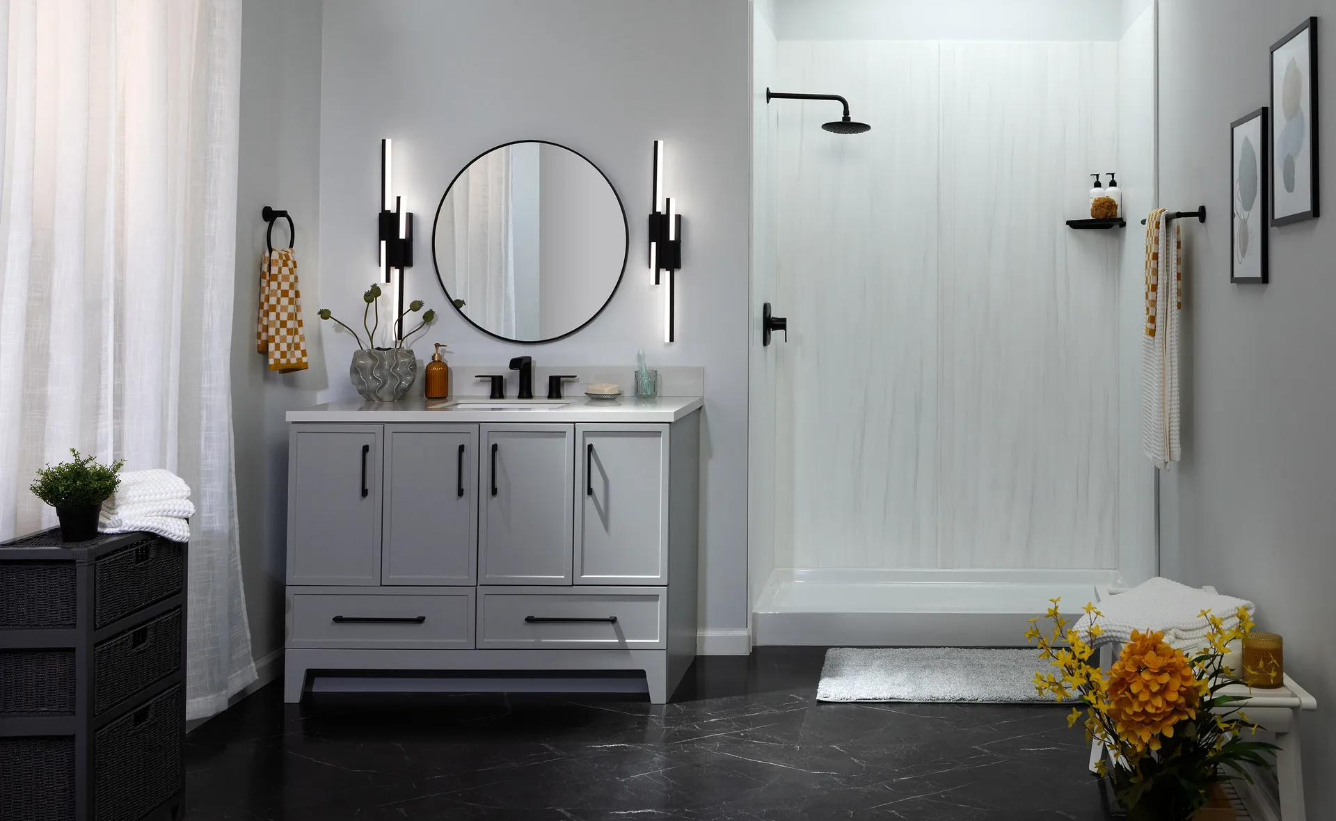 Modern bathroom with gray vanity, round mirror flanked by black sconces, walk-in shower with rainfall showerhead, and black marble flooring